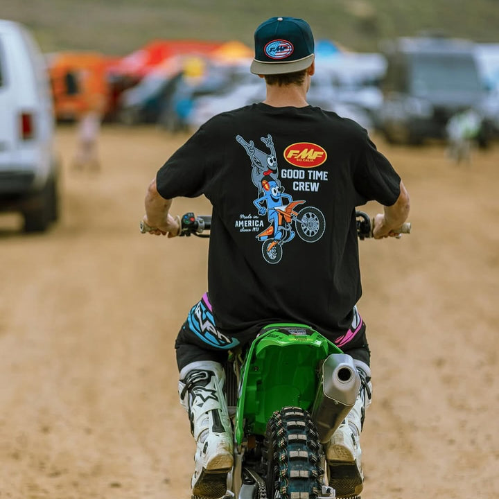 Person on a dirt bike wearing a black t-shirt with graphics and text, on a dirt track.