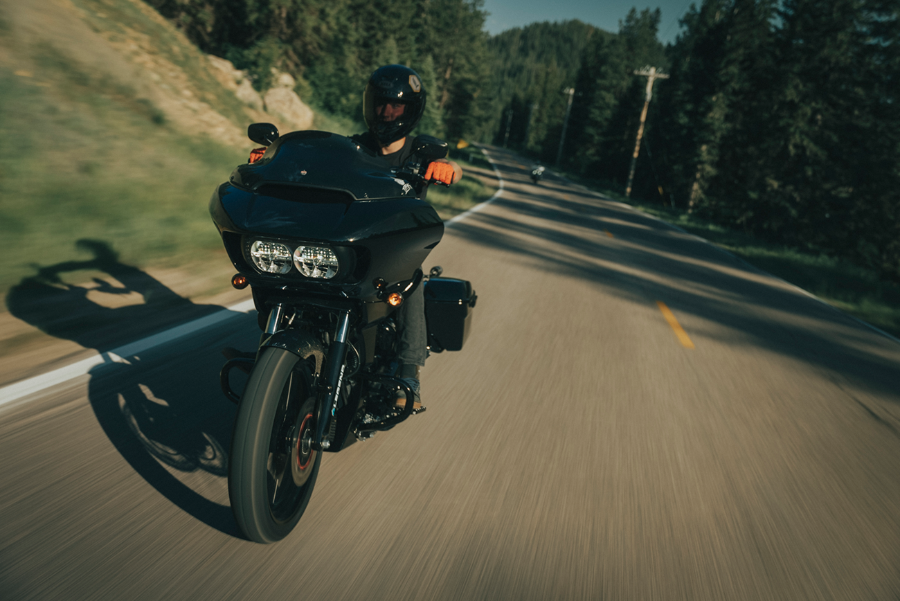 Person riding a black motorcycle on a road with trees in the background