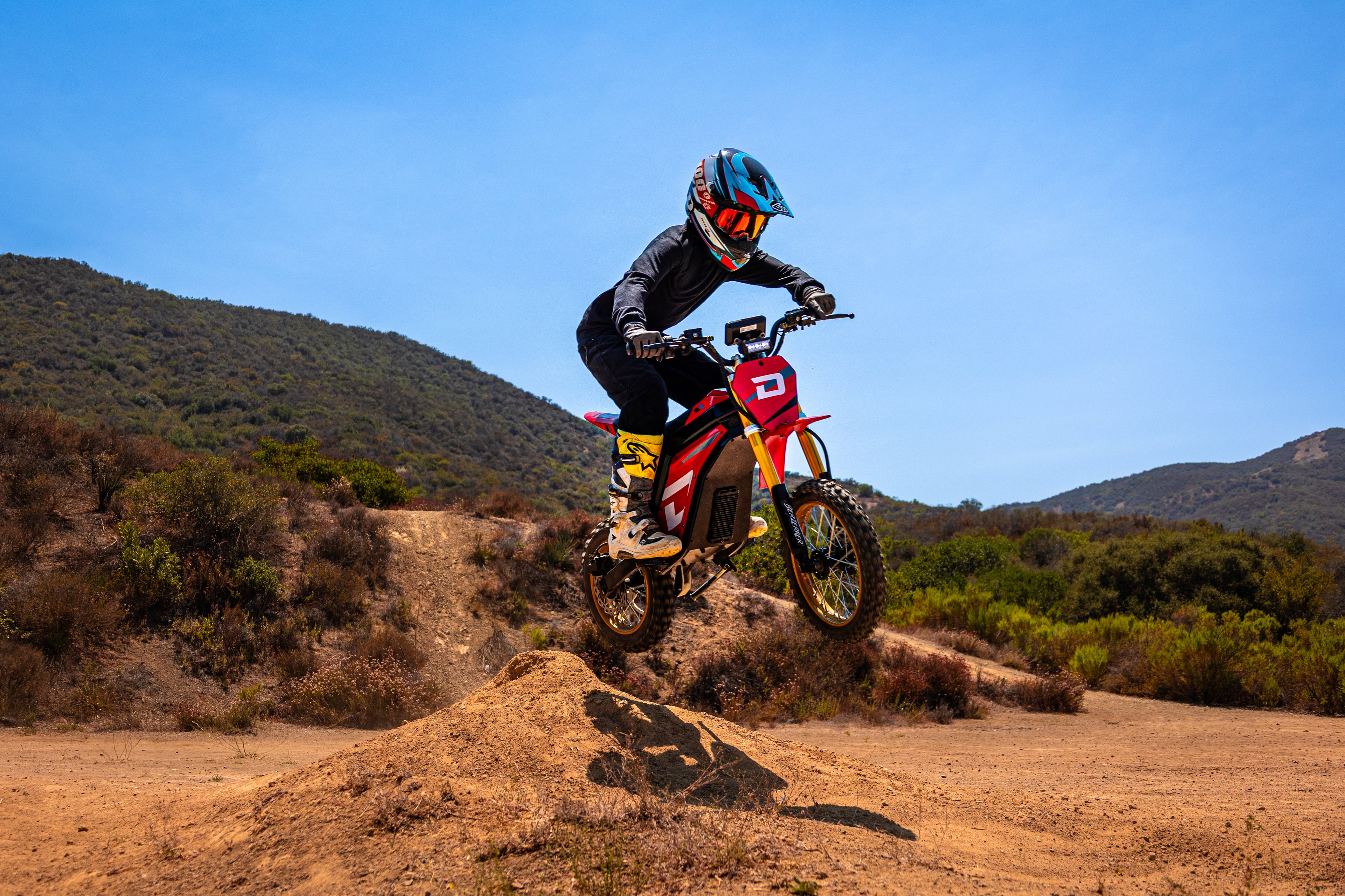 Person riding a dirt bike on a dirt track with mountains in the background