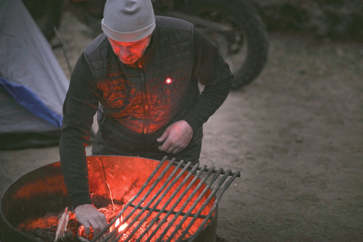 Person tending to a fire pit with glowing embers wearing a heated vest