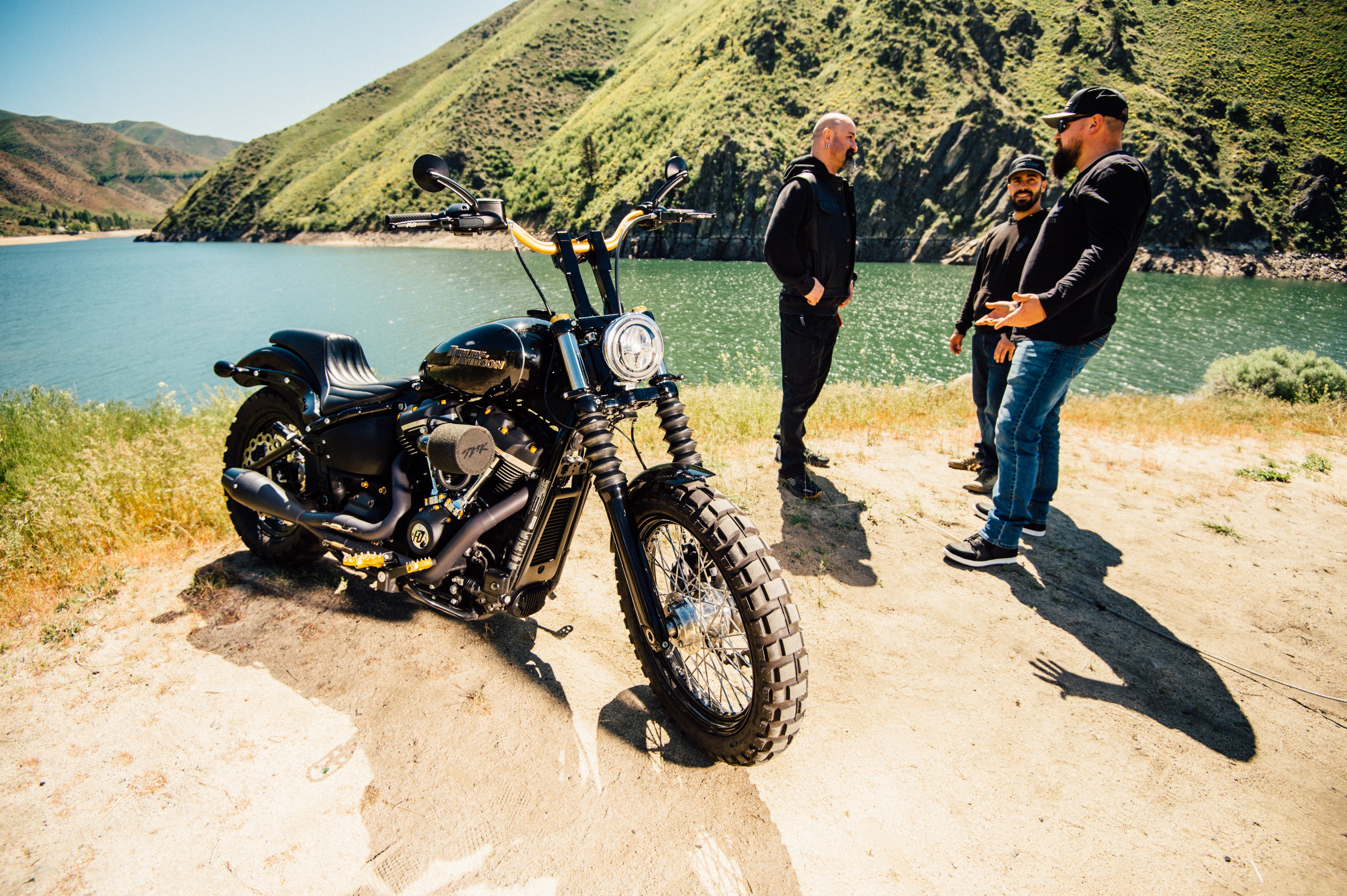 Motorcycle on a dirt road with people in the background near a scenic lake.