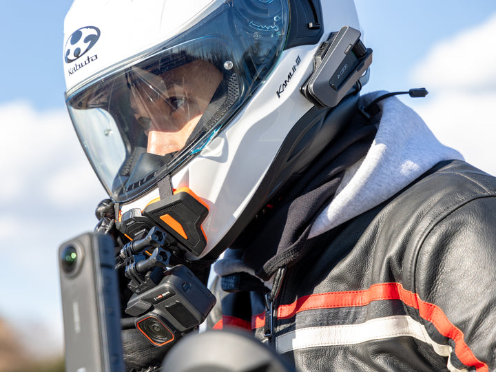 Person wearing a motorcycle helmet with communication device, outdoors.