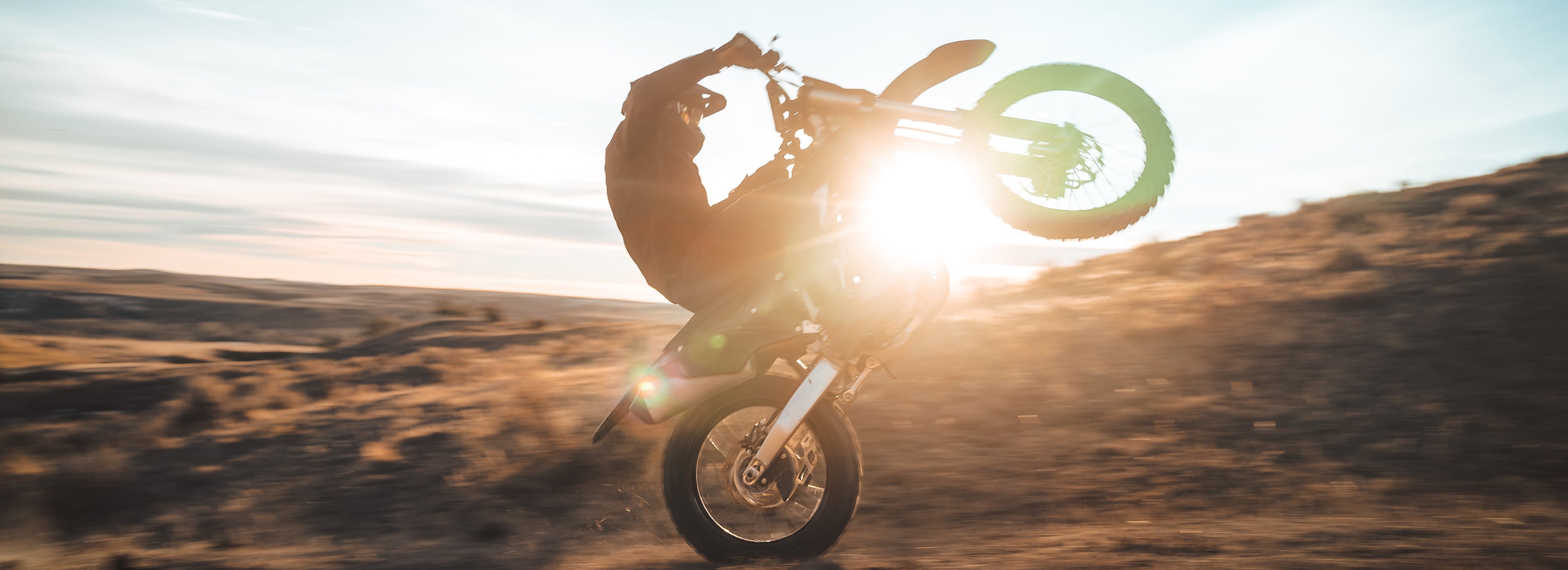 Person riding a motorcycle in the desert with the sun in the background