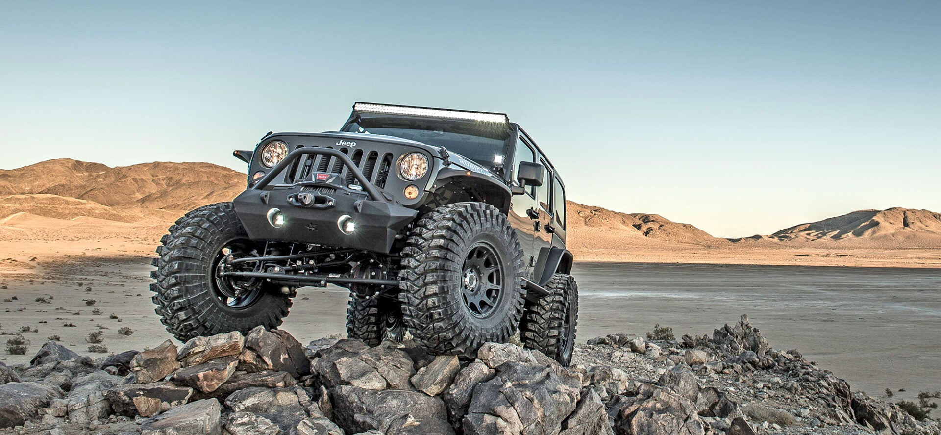 Black off-road vehicle on rocky terrain with a desert landscape in the background