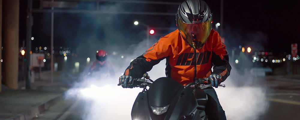 Man riding a motorcycle at night with a bright orange motorcycle jacket