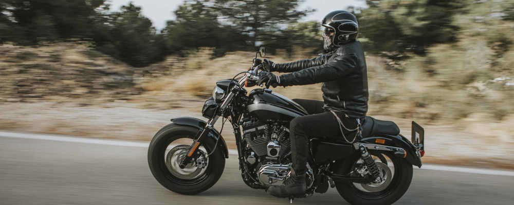 Man riding his all-black motorcycle with all-black gear (motorcycle helmet, jacket, gloves, pants, and boots)
